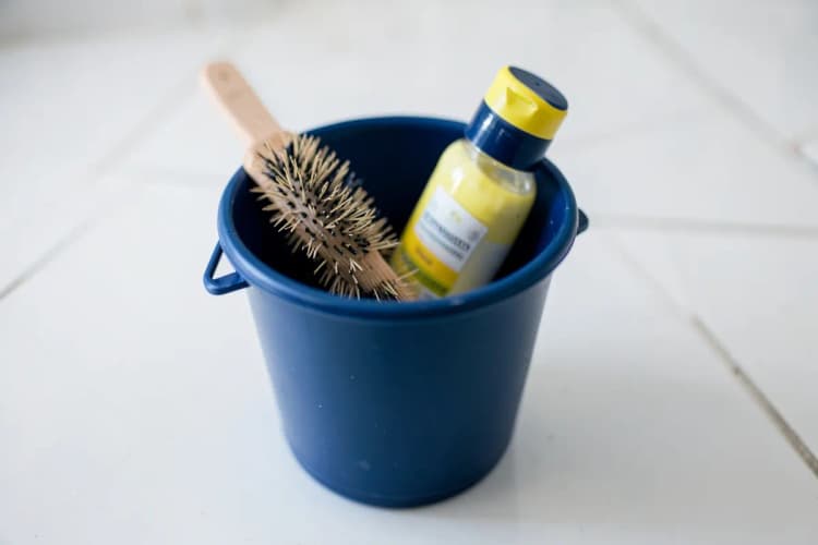 Um balde de plástico azul com uma escova de banho e um frasco de shampoo para cães ao lado.